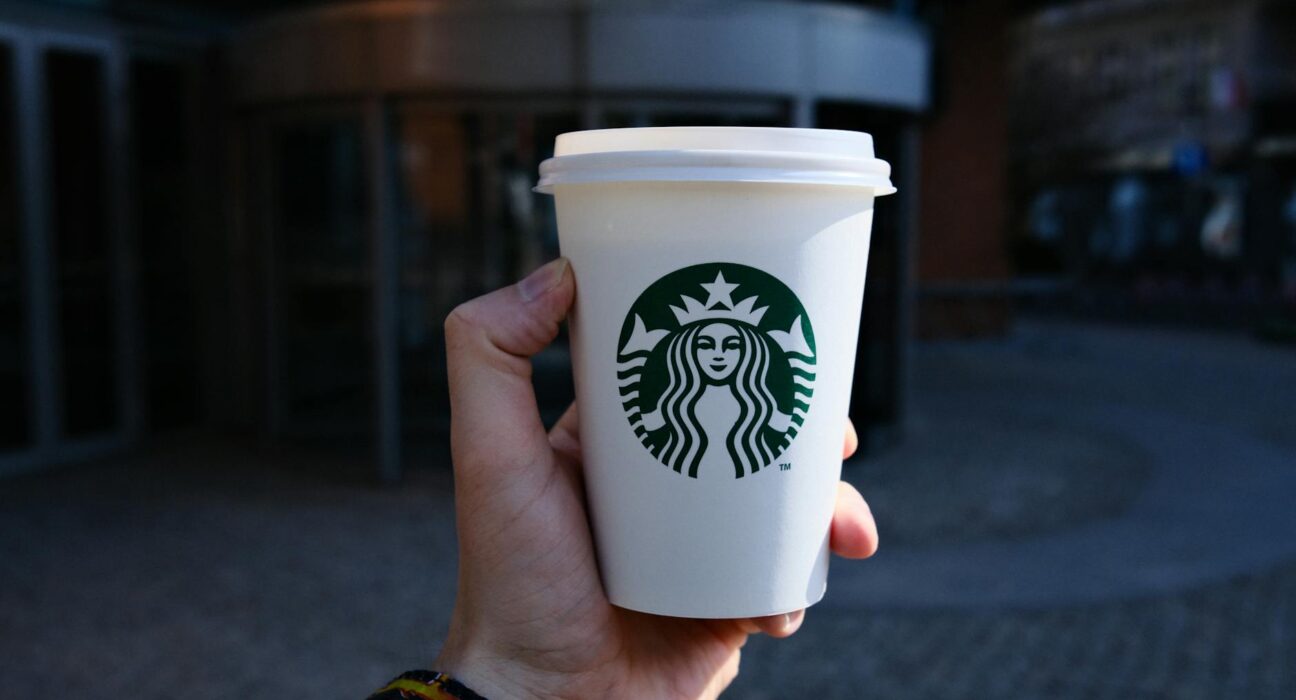 A hand holds a disposable coffee cup with a logo outdoors in Poznań, Poland.