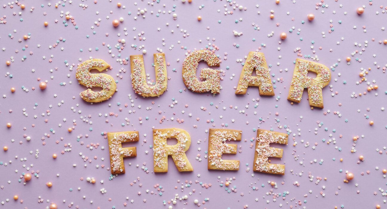 Flatlay of sugar-free cookie letters with sprinkles on a pink background.