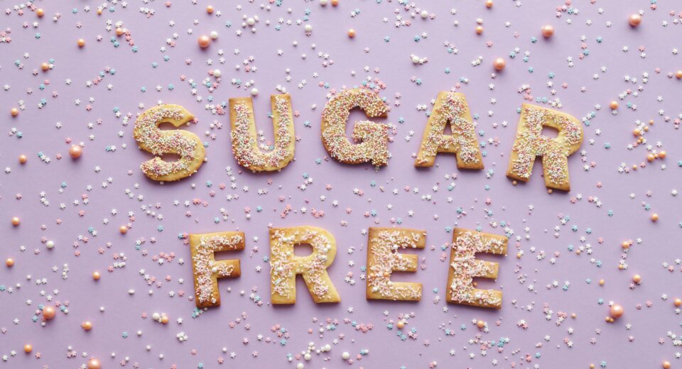Flatlay of sugar-free cookie letters with sprinkles on a pink background.