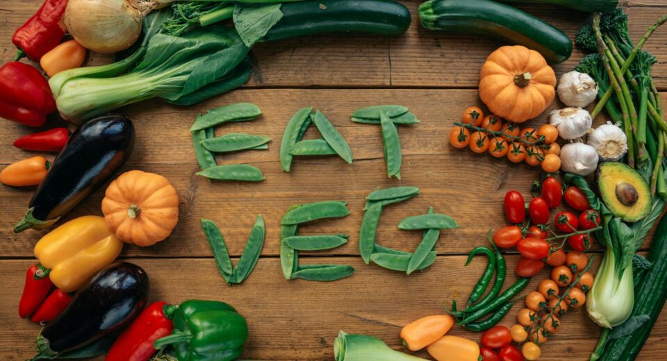 A vibrant flat lay of various fresh vegetables spelling 'Eat Veg' on a wooden background.