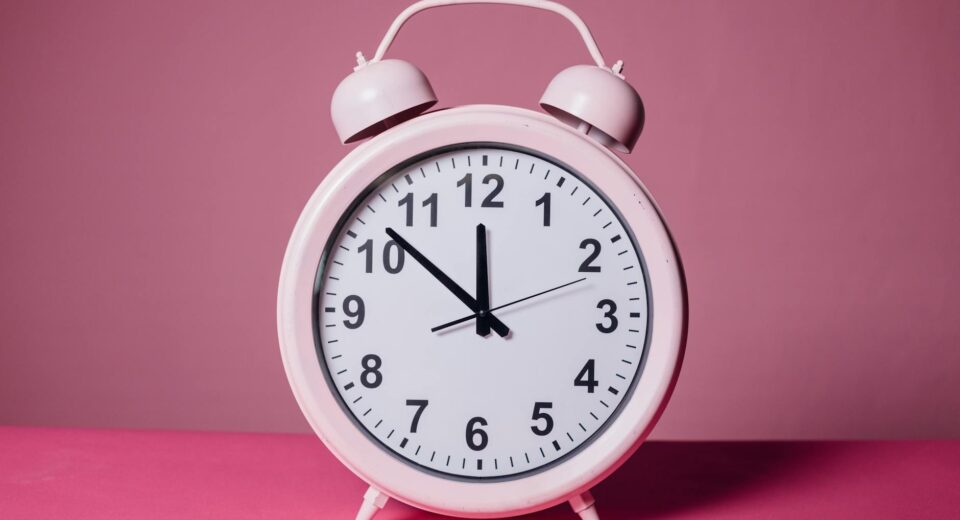 Pink retro alarm clock on a pastel pink background symbolizing time and punctuality.