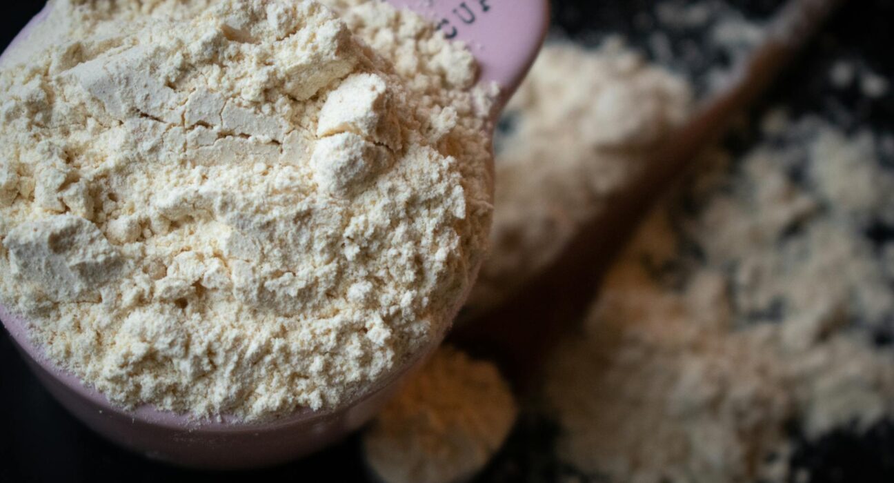 A filled measuring cup of flour spills onto a dark surface in a shallow depth of field.