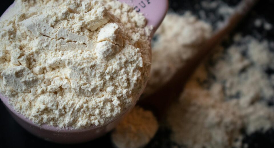 A filled measuring cup of flour spills onto a dark surface in a shallow depth of field.
