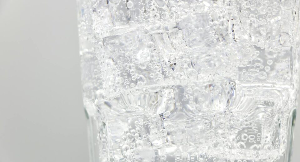 Refreshing sparkling water with ice cubes in a clear glass, close-up view.
