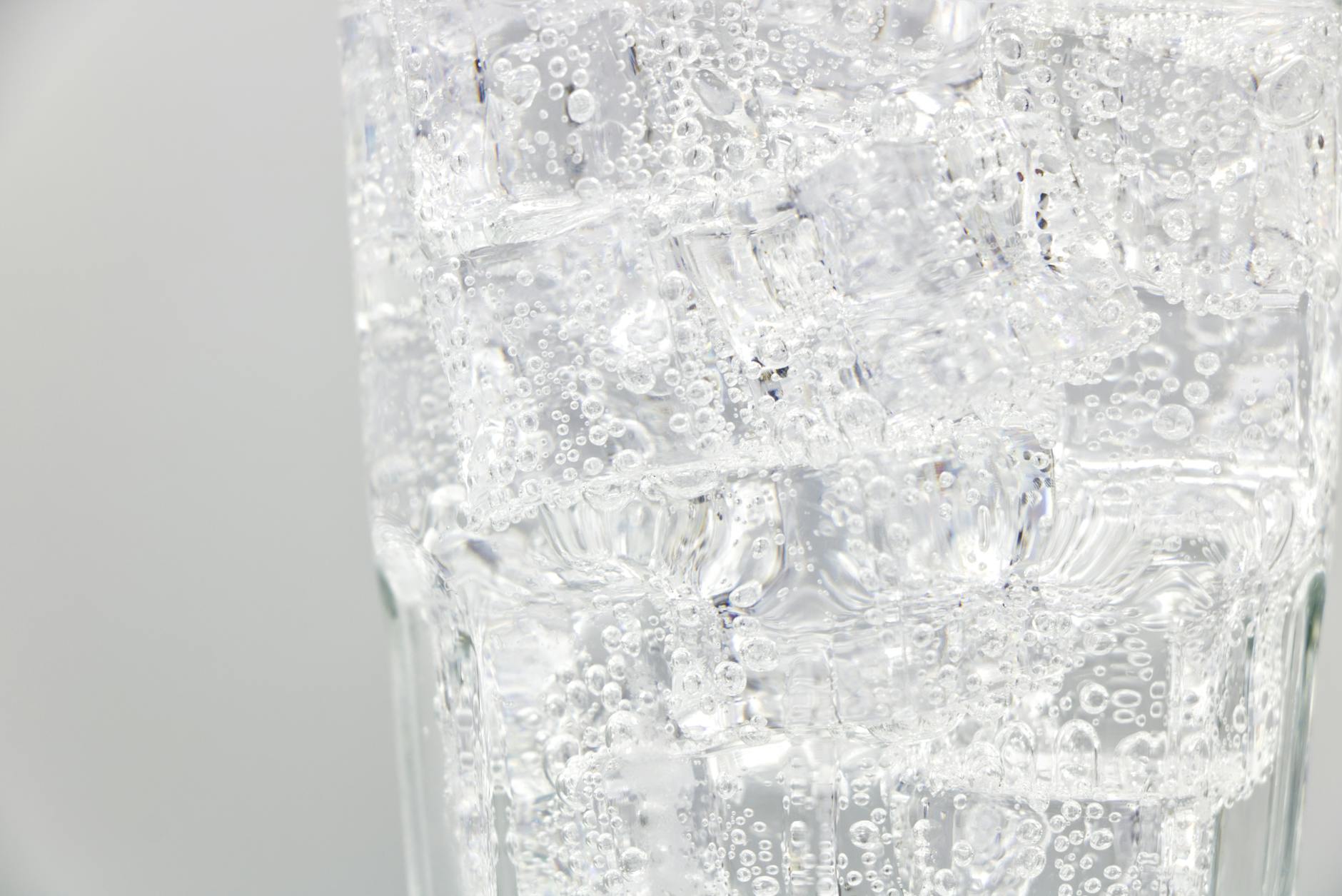 Refreshing sparkling water with ice cubes in a clear glass, close-up view.