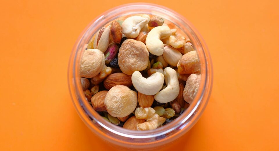 Close-up of a mix of nuts in a clear container against an orange background.