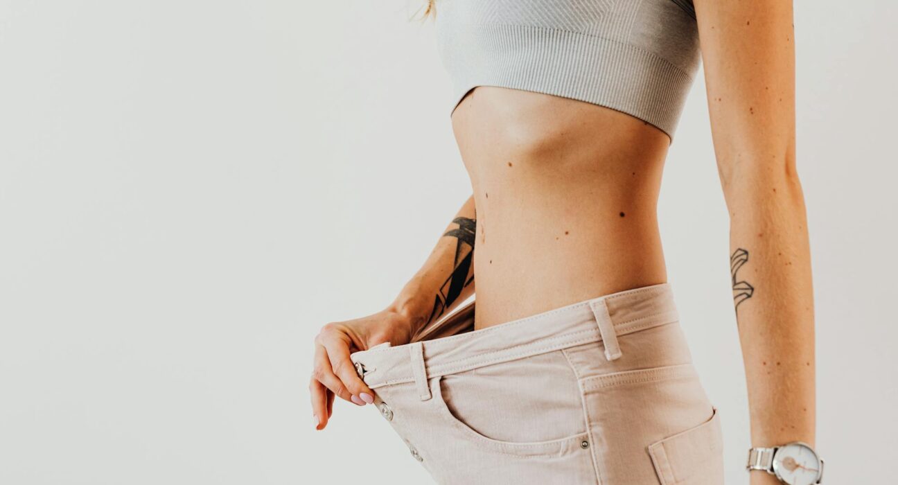Close-up of a woman in oversized jeans symbolizing weight loss in a studio setting.