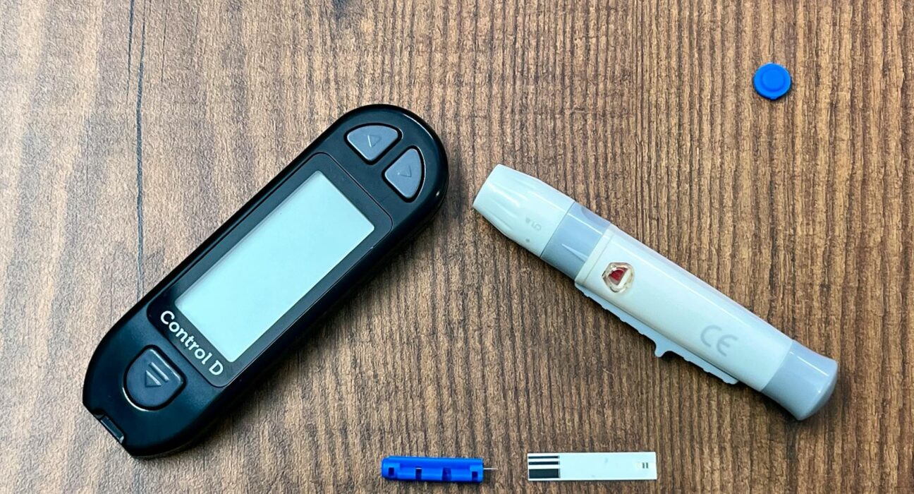 Close-up of a diabetes monitoring kit with glucometer and lancing device on a wooden surface.