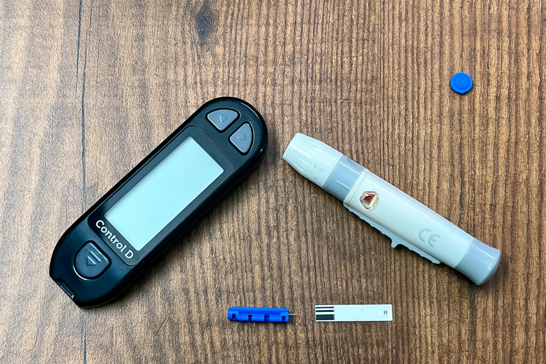 Close-up of a diabetes monitoring kit with glucometer and lancing device on a wooden surface.