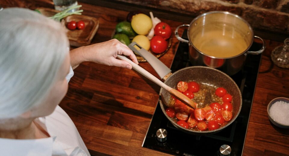 A senior woman prepares a homemade tomato sauce in a warm, cozy kitchen setting.