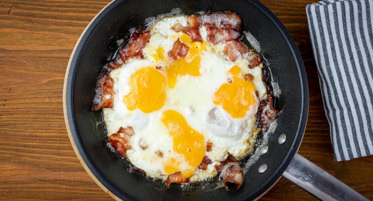 Sizzling bacon and sunny side up eggs in a frying pan, perfect for breakfast lovers.