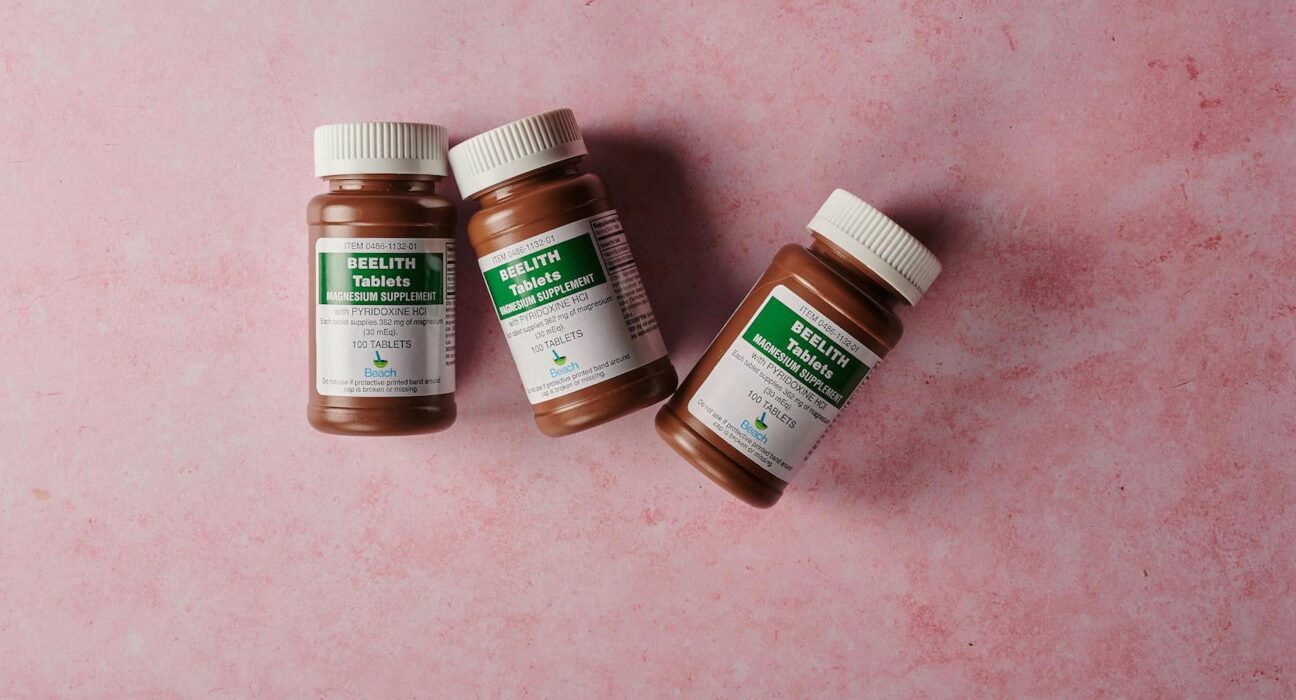 Three brown bottles of magnesium tablets on a soft pink background, ideal for health-themed content.