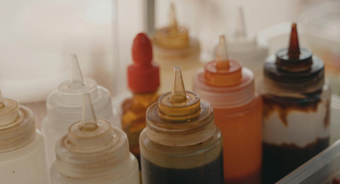 Close-up of various condiment squeeze bottles in a food preparation setting.