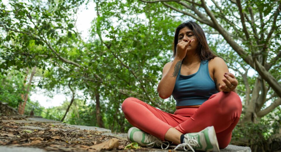 Young woman meditating in a forest, practicing yoga breathing exercises on a stone platform.