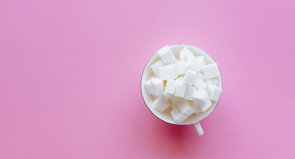 Top view of a cup filled with sugar cubes on a vibrant pink background.