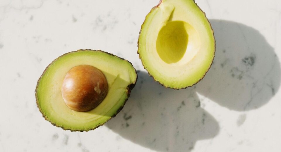Close-up of two fresh avocado halves on a marble surface, displaying vibrant green color and seed.