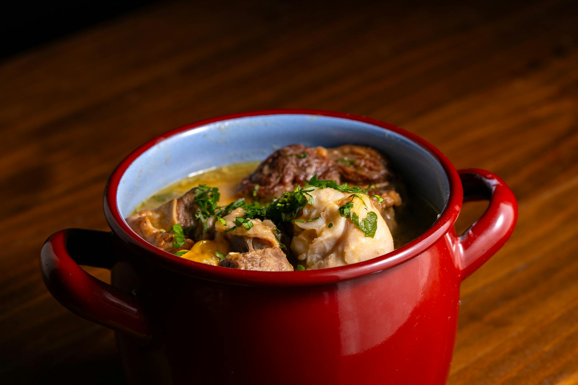 Warm and comforting hearty stew served in a rustic red pot on wood surface.