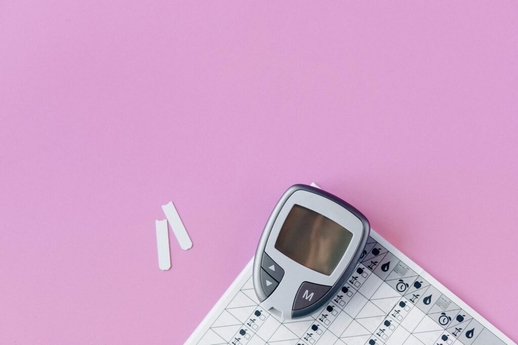 Flat lay of a blood glucose monitor and test strips on a pink surface.