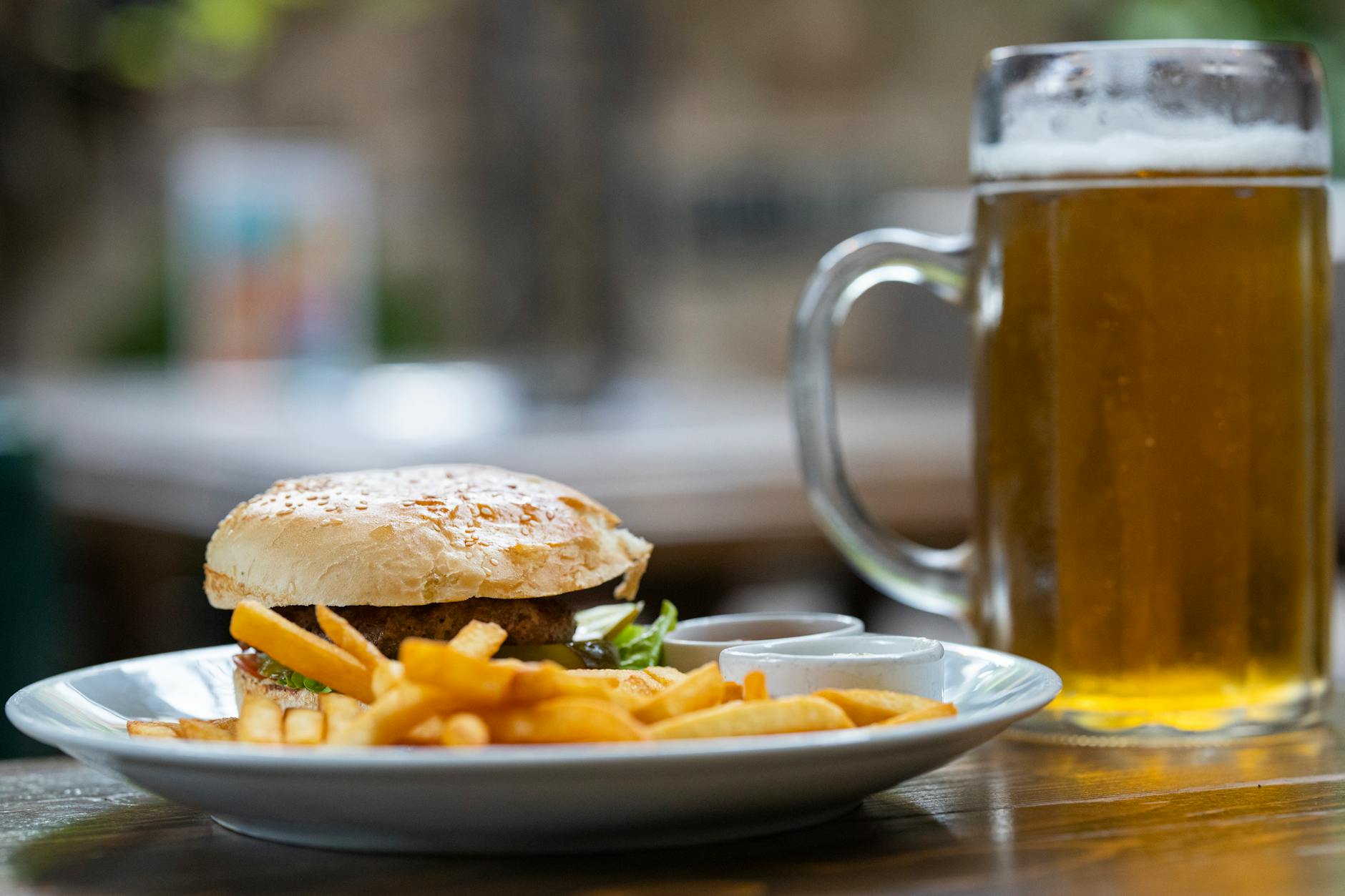 Mouthwatering burger with fries and a cold mug of beer on a plate outdoors.