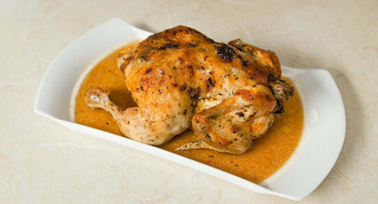 Perfectly roasted chicken on a white plate with savory gravy, ideal for food enthusiasts.