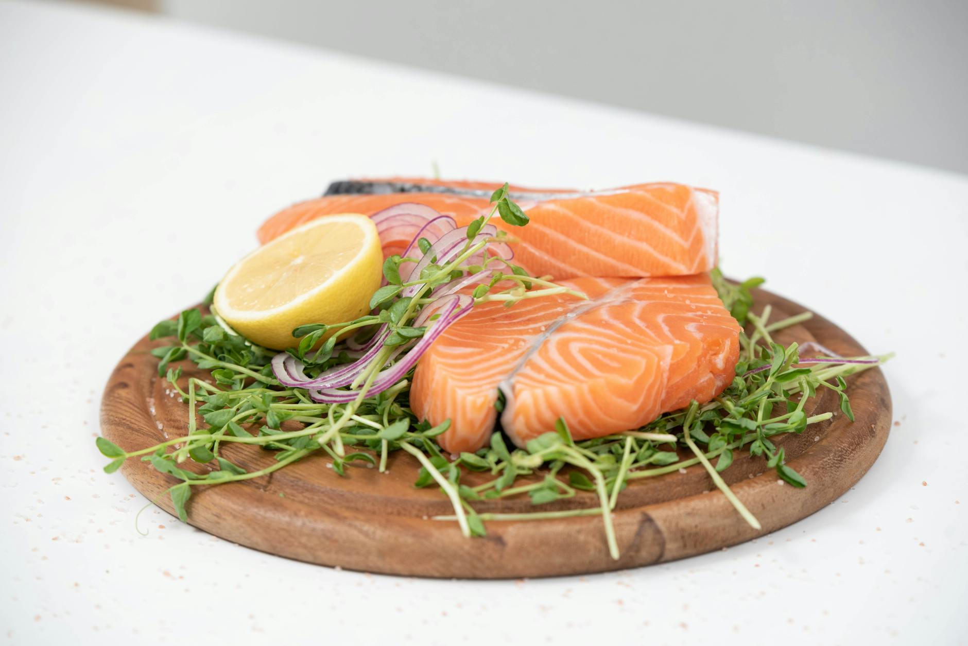 Close-up of fresh salmon slices with lemon and microgreens on a wooden platter. Ideal for food-related themes.