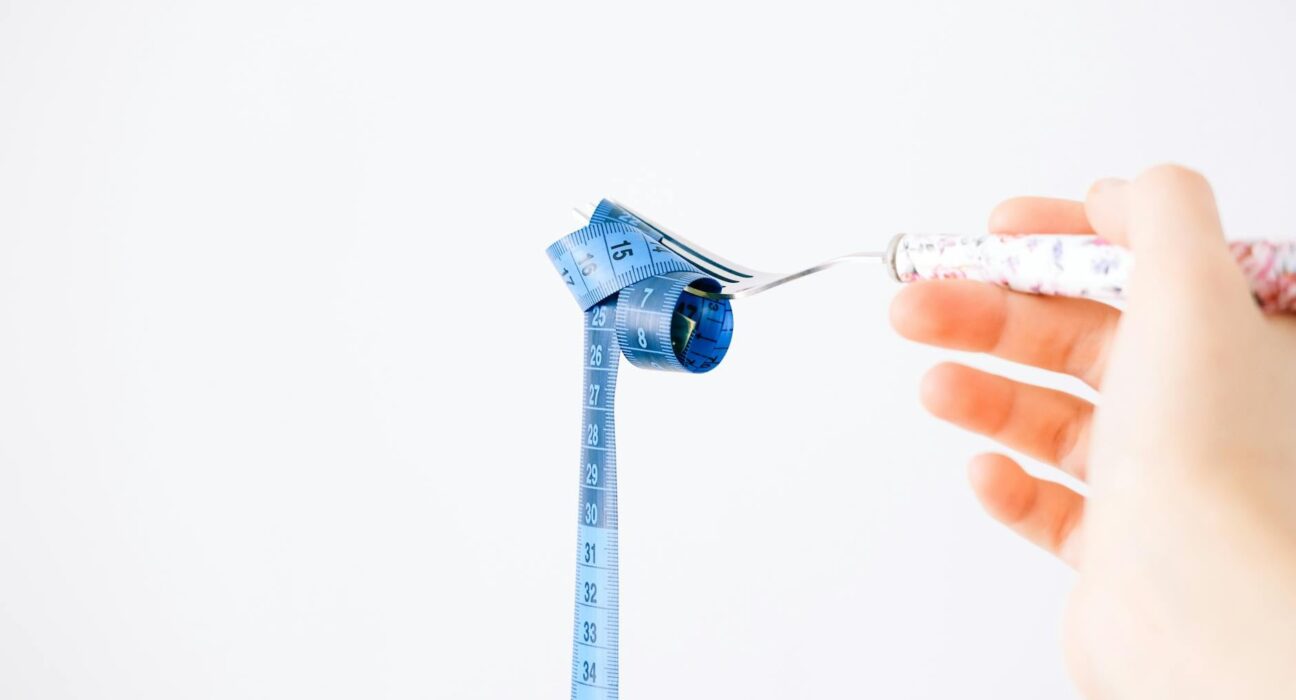 A blue measuring tape wrapped around a fork representing dieting or healthy eating concept.