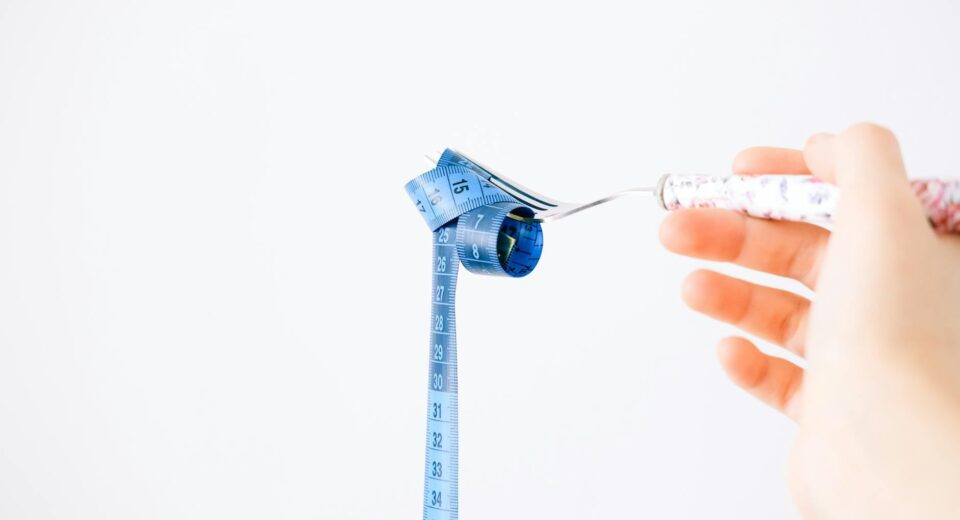 A blue measuring tape wrapped around a fork representing dieting or healthy eating concept.