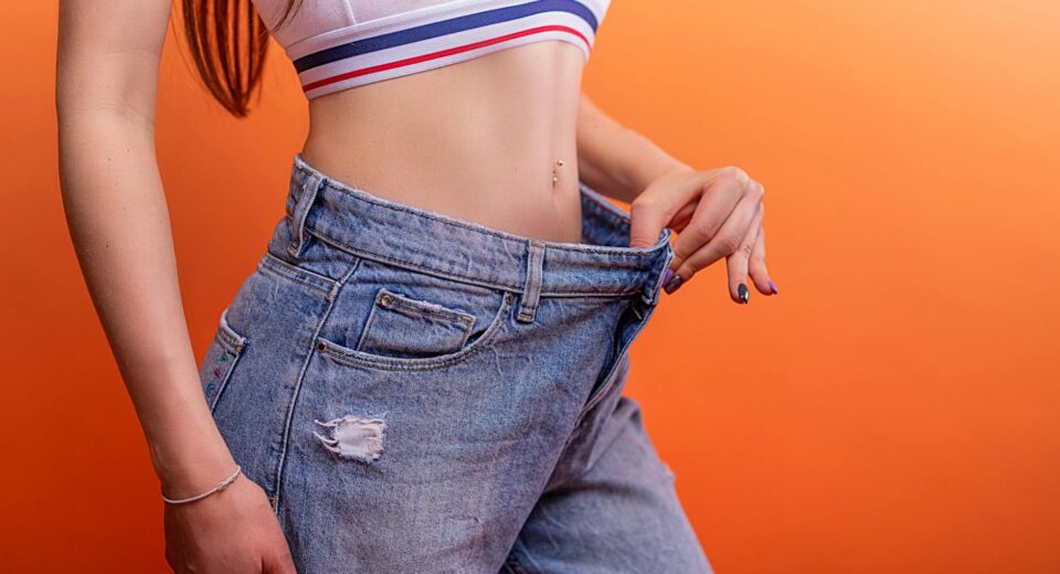 A woman holding loose jeans against her slim waist, symbolizing successful weight loss.