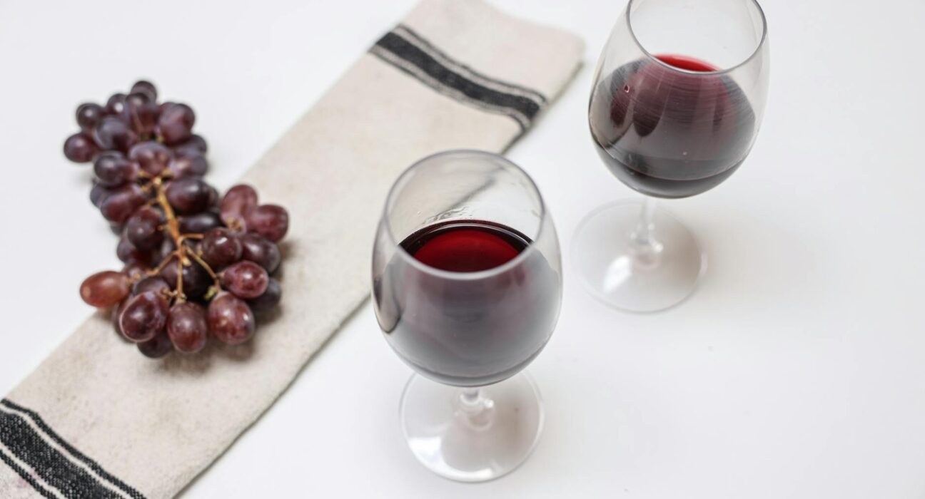 Two wine glasses and a bunch of grapes elegantly arranged on a white table with a napkin.